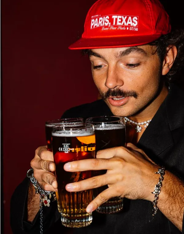 Hombre con gorra roja sosteniendo tres vasos de cerveza